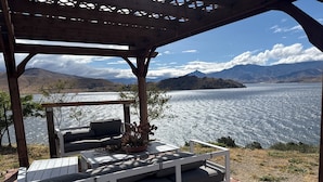 Un espacio de estar al aire libre techado, con vistas a un lago y montañas.