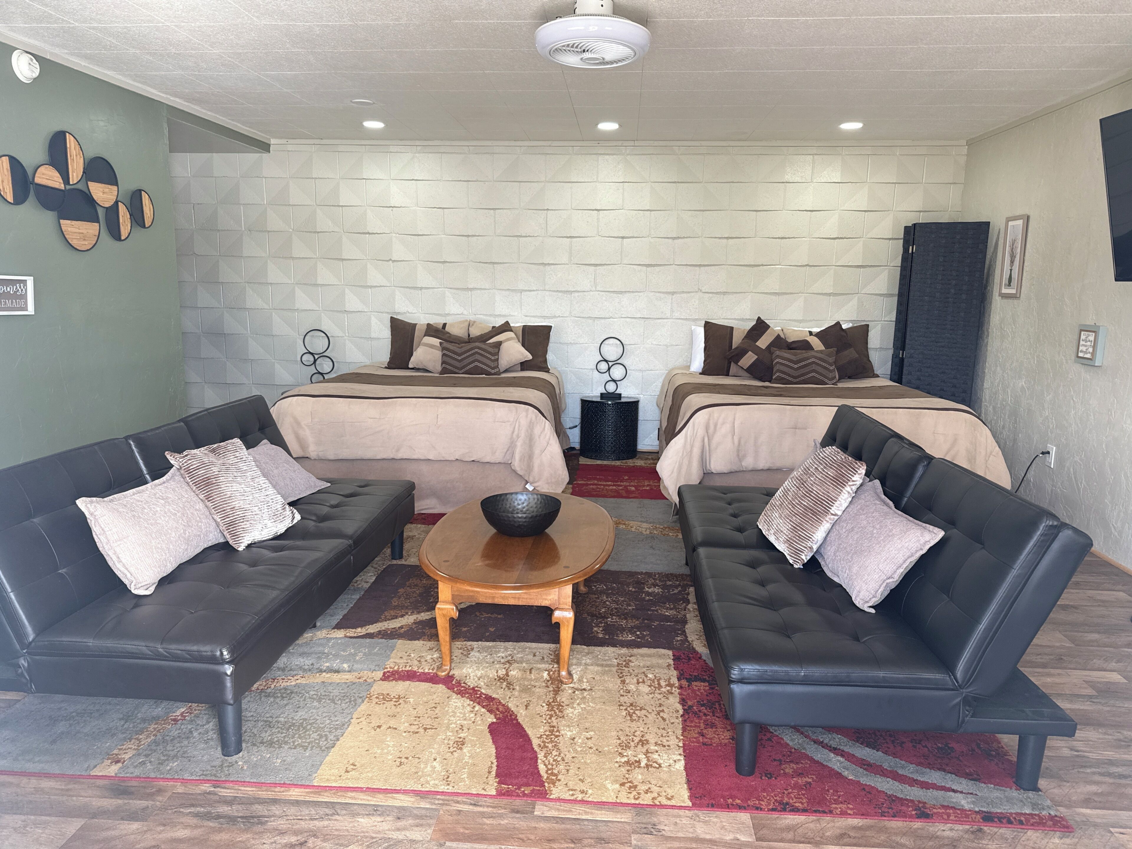 A room with two beds, two black leather sofas, a wooden coffee table, and a patterned rug.
