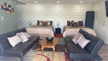 A room with two beds, two black leather sofas, a wooden coffee table, and a patterned rug.