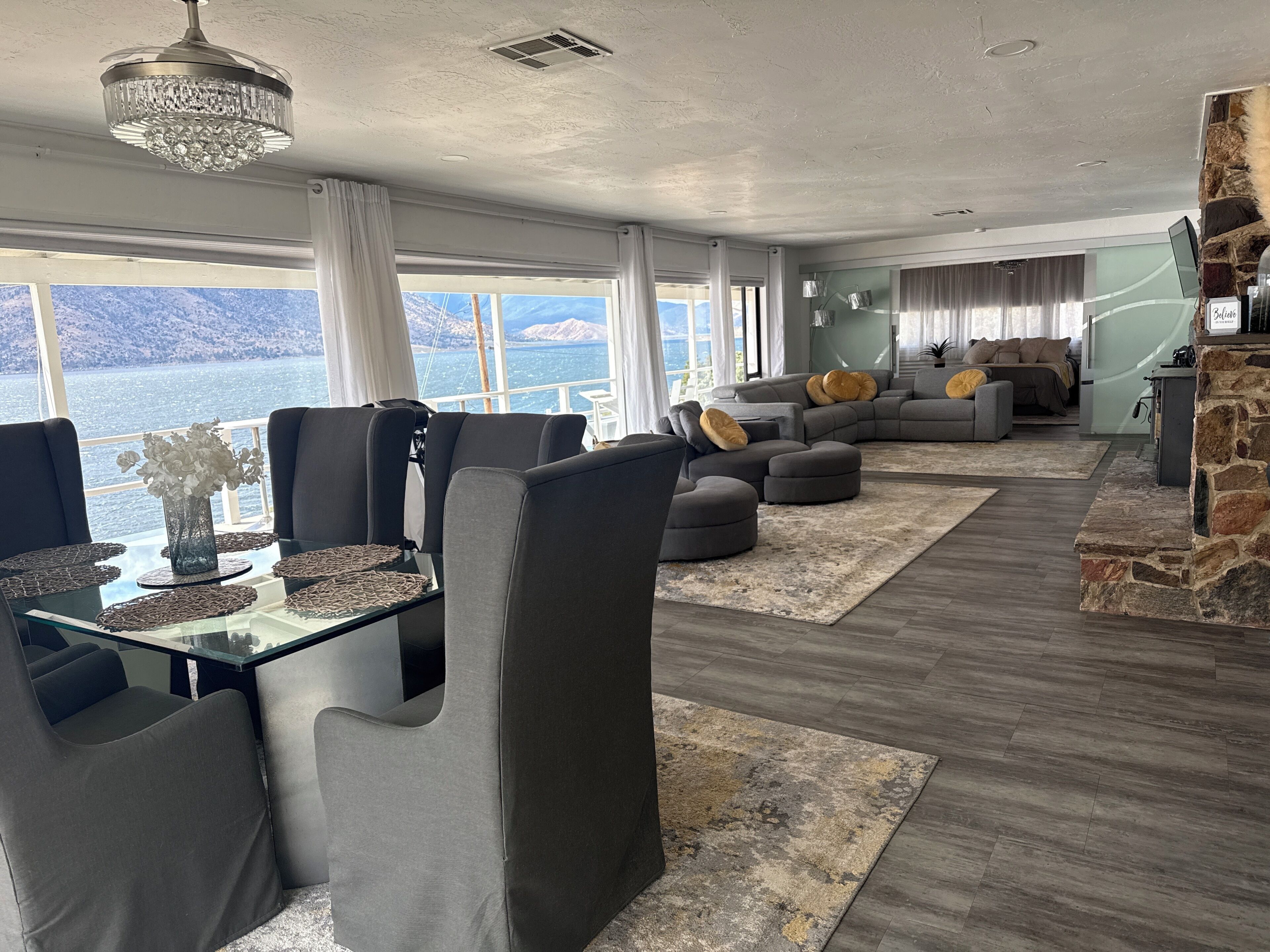 Una sala de estar moderna con comedor, chimenea de piedra y un amplio ventanal con vista al agua.