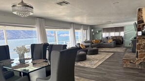 Una sala de estar moderna con comedor, chimenea de piedra y un amplio ventanal con vista al agua.