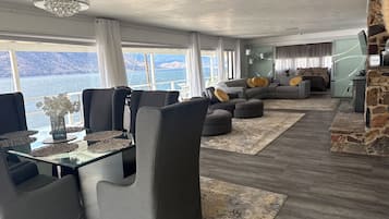 Una sala de estar moderna con comedor, chimenea de piedra y un amplio ventanal con vista al agua.