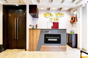 A reception desk labeled 'TOWNHOUSE' with a 'Company-Served' sign, a wooden door, a wall-mounted fan, and a decorative wall piece. - Premium New Krish Residency (Barasat)