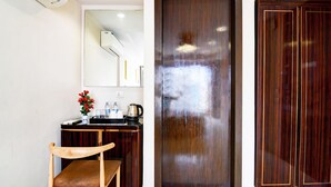 A room with a wooden chair, a small table with a flower vase, a mirror, a wooden wardrobe, and a door. - Premium New Krish Residency (Barasat)