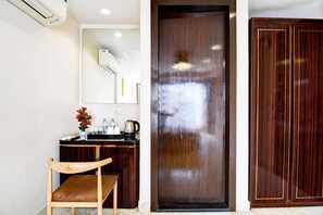 A room with a wooden chair, a small table with a flower vase, a mirror, a wooden wardrobe, and a door. - Premium New Krish Residency (Barasat)