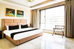 Una camera d'albergo con un letto grande, un comodino, una finestra con tende e due opere d'arte appese alle pareti.