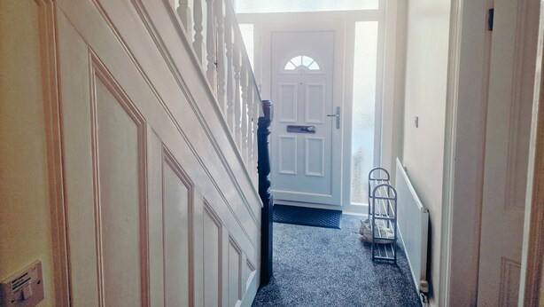 A hallway with a staircase, a door with a window, and a radiator.