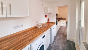 A modern kitchen with white cabinets, a wooden countertop, a washing machine, and a visible fire extinguisher.