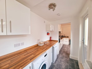 A modern kitchen with white cabinets, a wooden countertop, a washing machine, and a visible fire extinguisher. - Bright Modern 4-Bed Home Minutes from Anfield (Liverpool)