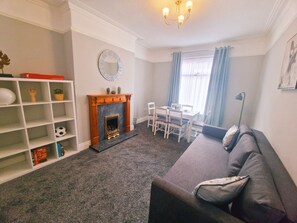 A living room with a fireplace, a sofa, a dining table with chairs, and a bookshelf.