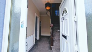 A hallway with a carpeted floor, a wooden door, and a light fixture.
