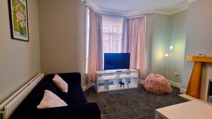 A living room with a dark-colored sofa, a white TV stand, a pink ottoman, and a small table.