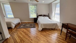 Quarto com duas camas, um ventilador de teto, piso de madeira e uma janela.