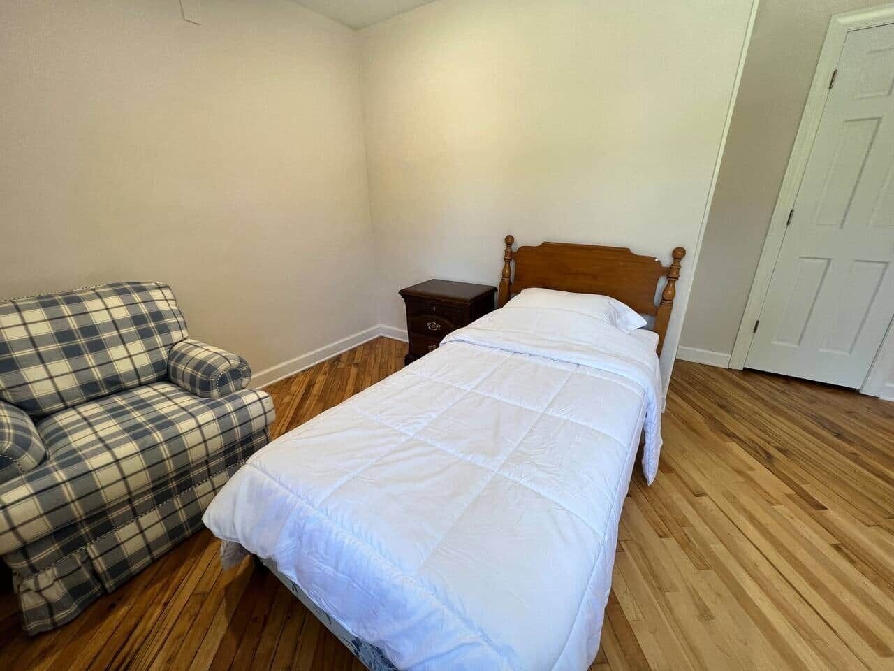 A bedroom with a bed, a wooden nightstand, a plaid sofa, and a white door.