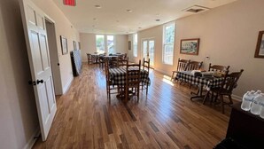 Een ruime eetruimte met houten vloeren, meerdere tafels met geruit tafelkleed en stoelen.