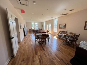 A spacious dining area with wooden flooring, multiple tables with checkered tablecloths, and chairs.