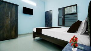 Ett hotellrum med en säng, en garderob, en tv, en luftkonditioneringsanläggning och en vas med blommor.