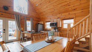 Une cabane en bois comprenant un coin repas, une cuisine et un escalier.