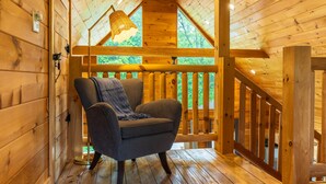 L’intérieur d’un chalet en bois, avec une chaise, un plafond en bois et une fenêtre donnant sur un paysage verdoyant.