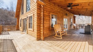 Une cabane en rondins avec une terrasse, des fauteuils à bascule et un espace barbecue.