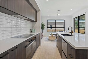 A modern kitchen with a central island, a large window, and a view of a brick building. - Neiwand Residence by Arvia Living (Calamvale)