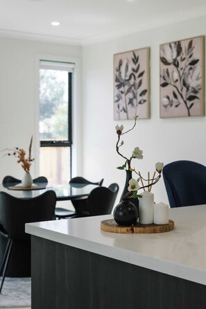 A modern dining area with a central island, black chairs, and a vase with flowers. - Neiwand Residence by Arvia Living (Calamvale)