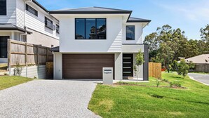 Une maison moderne à deux étages, dotée d’un garage, d’une allée et d’une pelouse bien entretenue.
