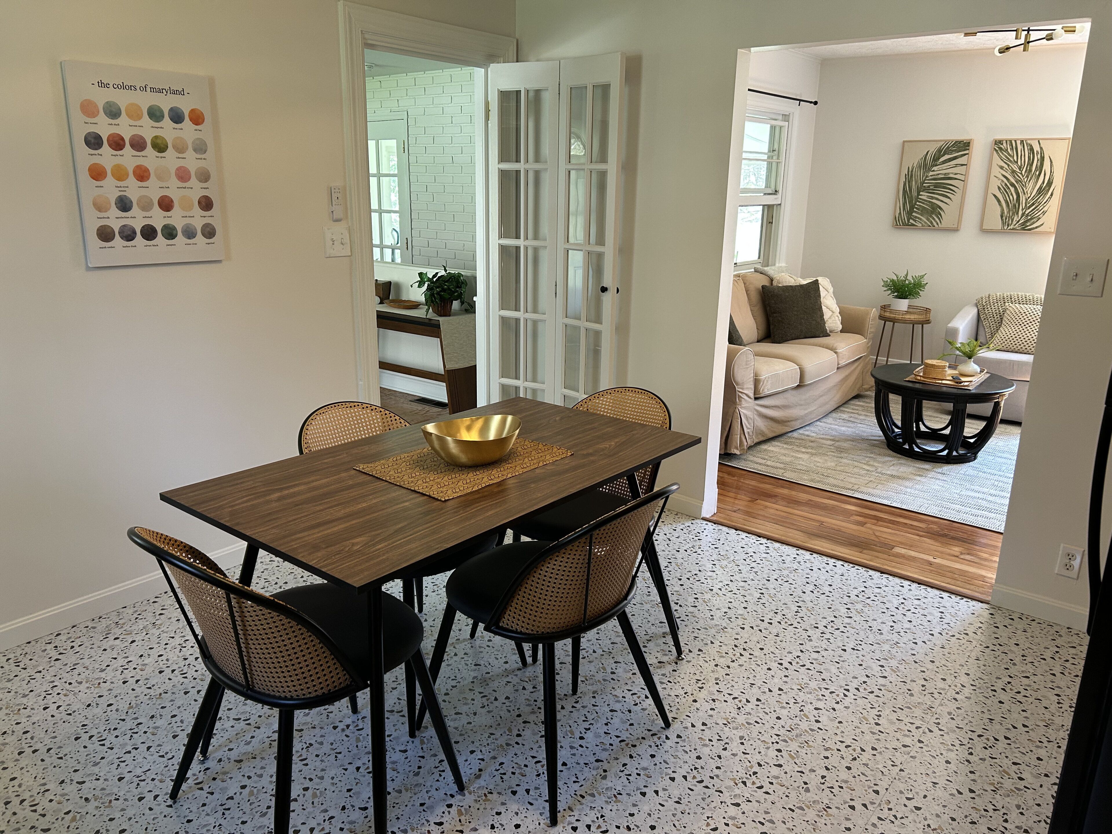 Een eetgedeelte met een houten tafel, vier stoelen, een gouden schaal en een stippen vloer.