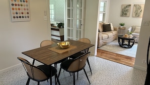 Uma sala de jantar com uma mesa de madeira, quatro cadeiras, uma tigela dourada e um chão estampado.