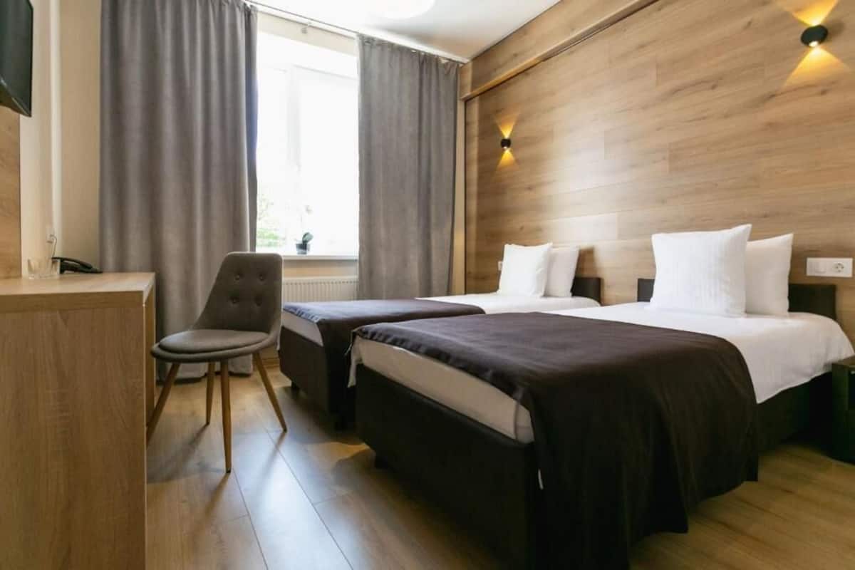 A hotel room with two beds, a desk, a chair, and a window with curtains.