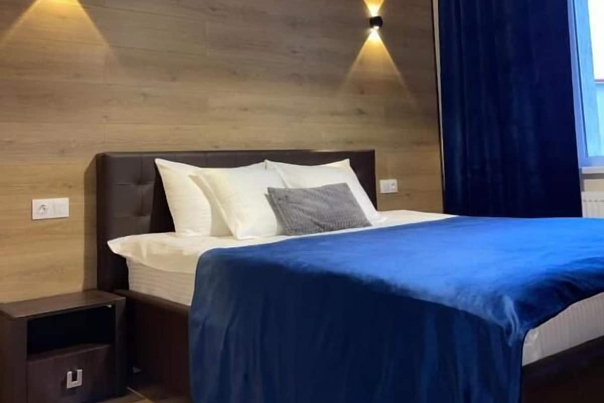 A modern bedroom with a bed, bedside tables, and wall-mounted lighting.