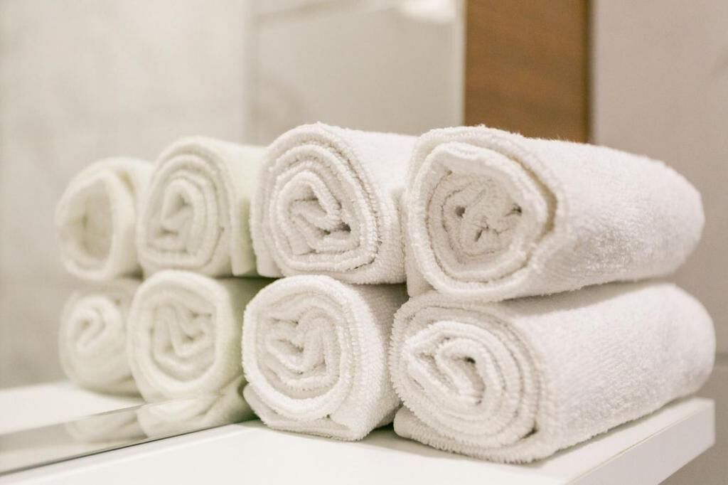 A stack of neatly rolled white towels on a white shelf.