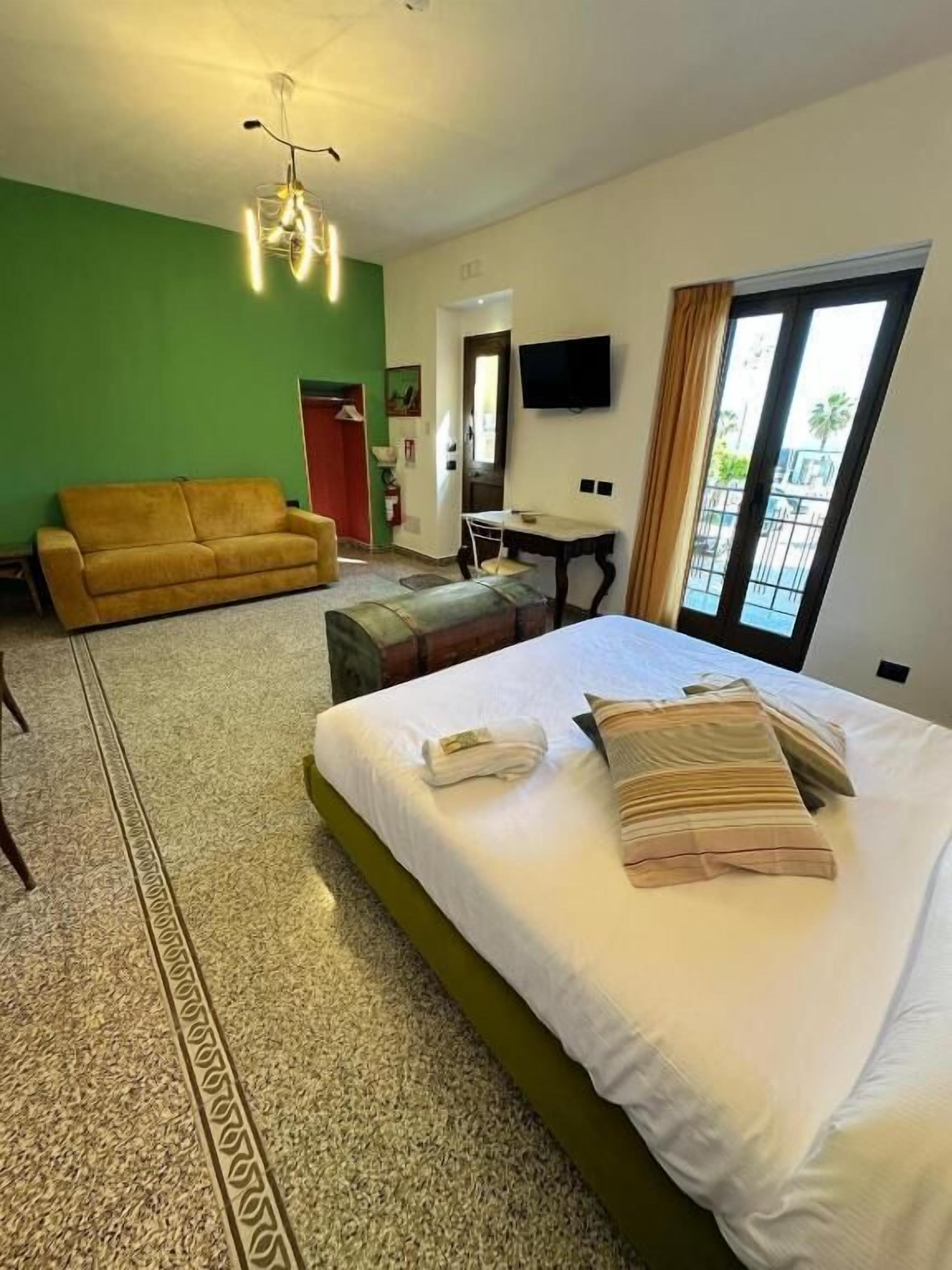 Habitación de hotel con cama, sofá, mesa de comedor, televisión y balcón.