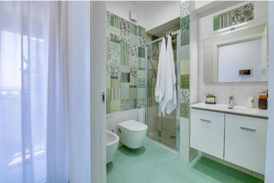 A bathroom with a toilet, bidet, and shower area, with patterned tiles and a white sink.