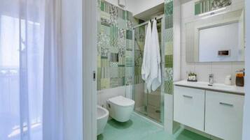 A bathroom with a toilet, bidet, and shower area, with patterned tiles and a white sink.