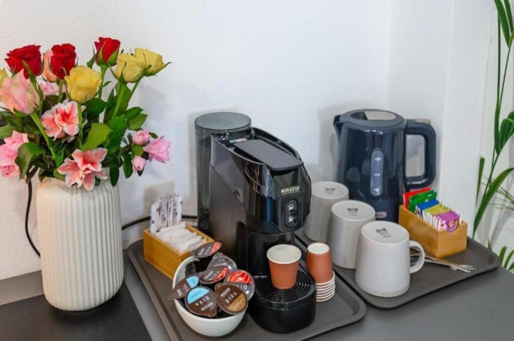 Estación de café con cafetera, tazas y una bandeja con cápsulas de café.