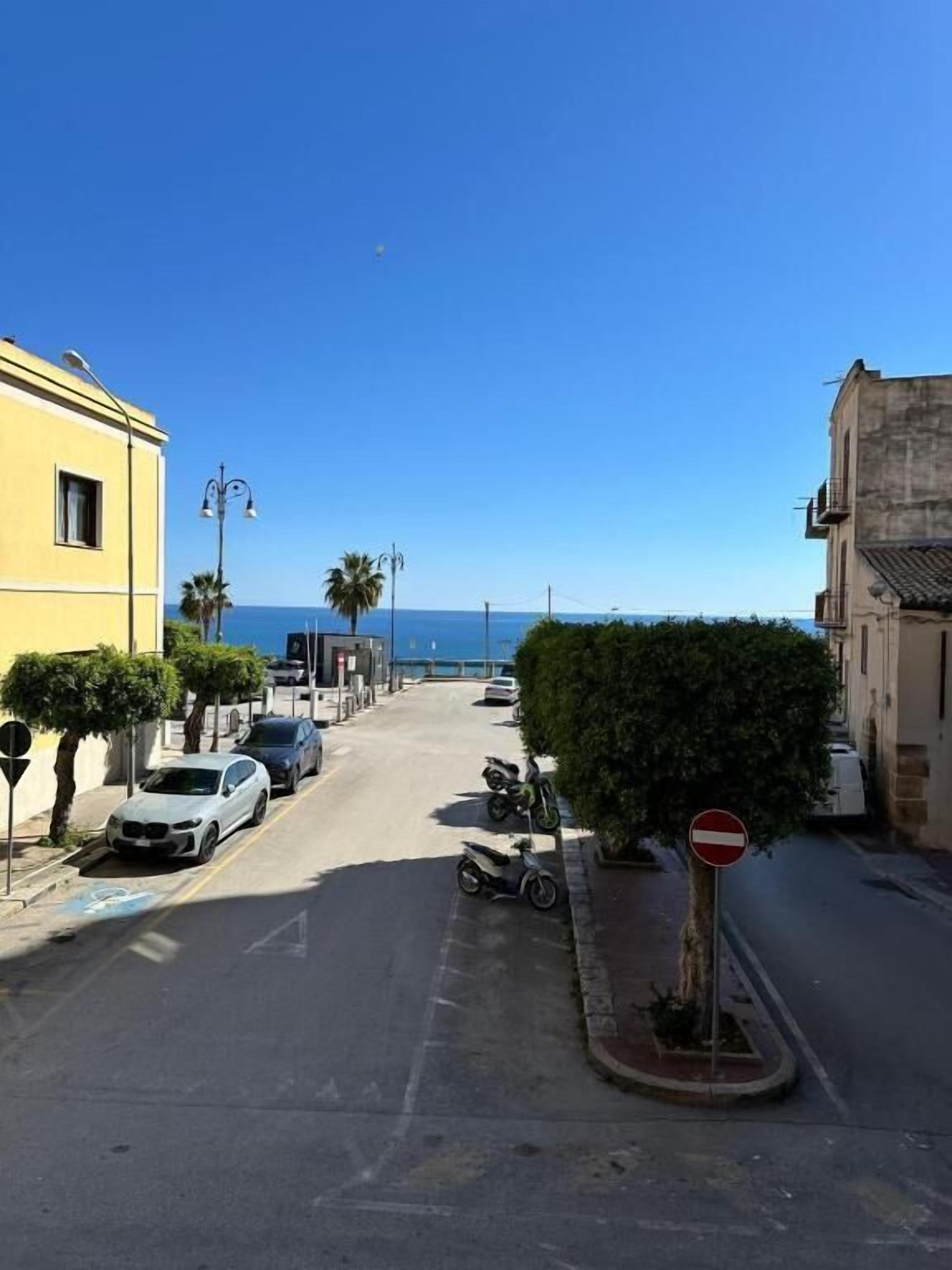 A street with parked cars and a no entry sign, leading to a body of water.
