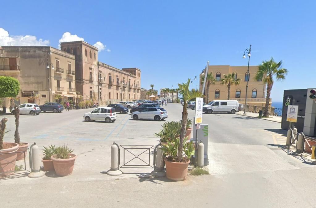 A street with parked cars, buildings, and palm trees.