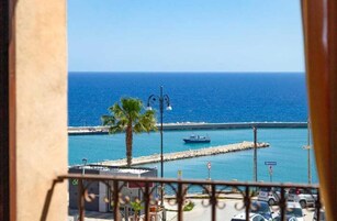 Un balcone con vista sul mare, una palma e una barca.