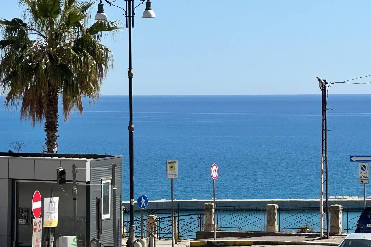 Una calle costera con una palmera, farolas, un coche y vista al mar.