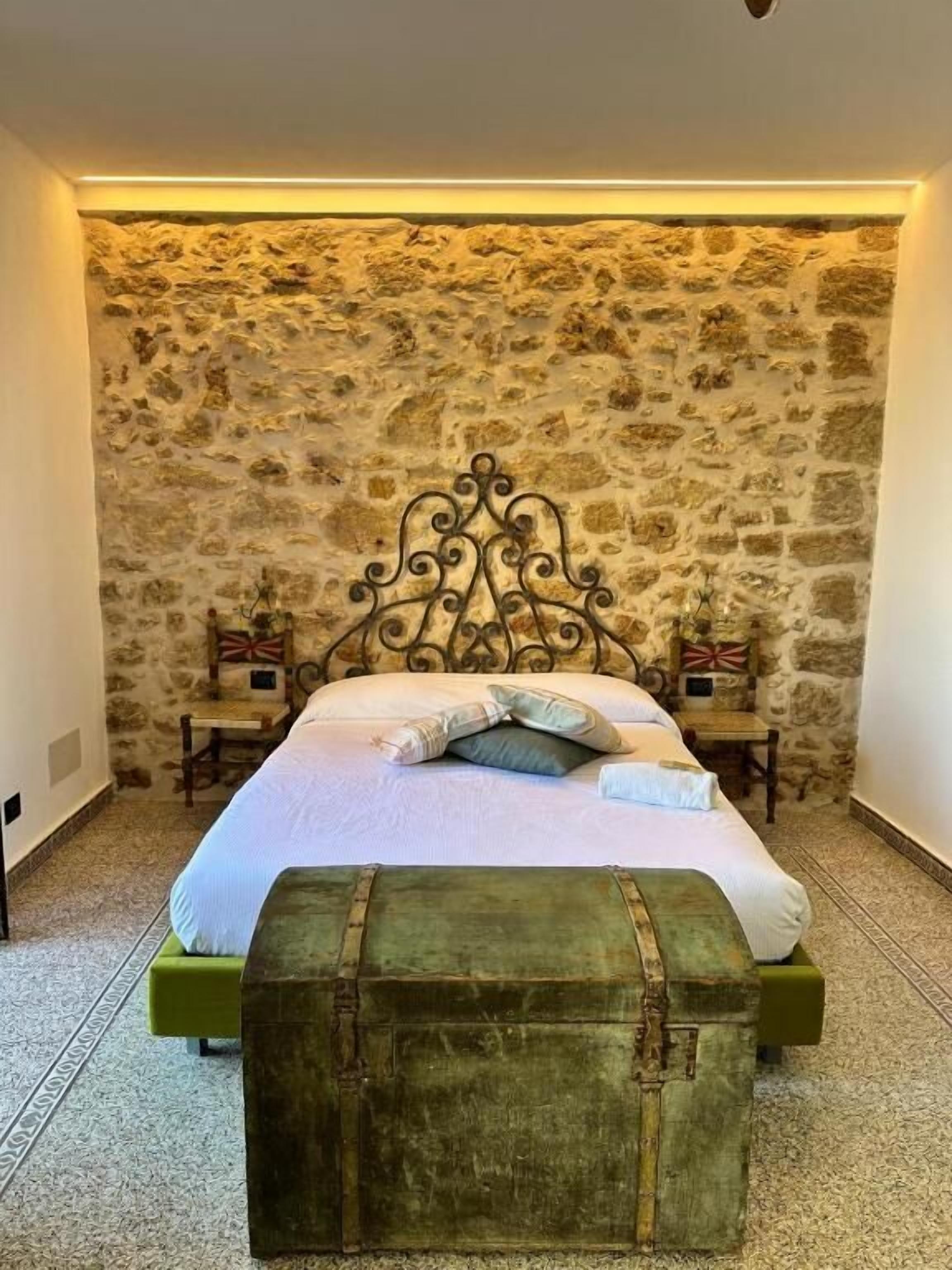 A bed with a stone wall backdrop, a green chest, and two bedside tables with flags.