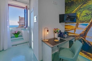 Una stanza con una scrivania, una sedia, TV e vista sul mare attraverso una finestra.