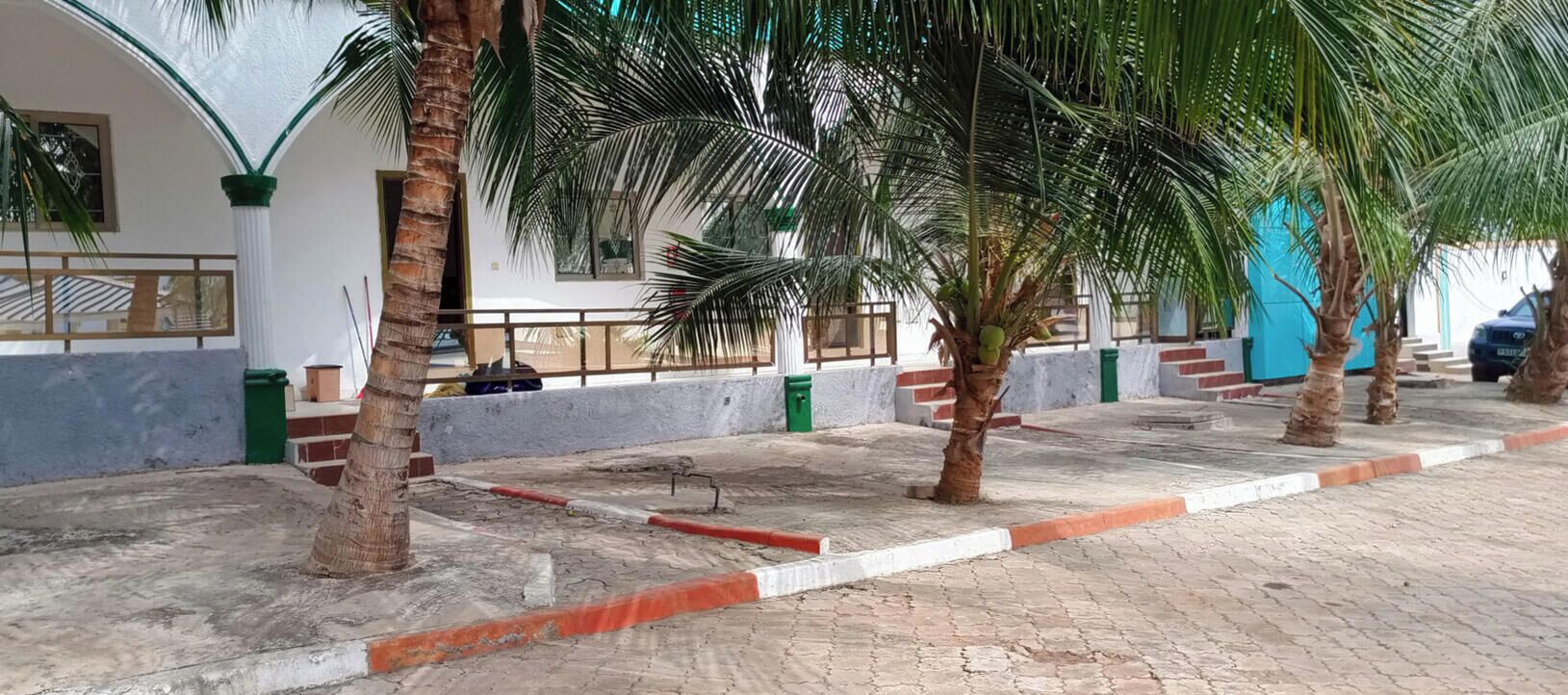 A paved outdoor area with palm trees, a blue building, and a car parked nearby.