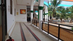 Un pasillo con columnas blancas, un extintor y vistas a palmeras y un edificio con fachada azul y naranja.