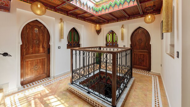 A room with a wooden door, a balcony with a wrought iron railing, and a patterned ceiling. - RIAD SULTAN CHEFCHAOUEN (Chefchaouen)