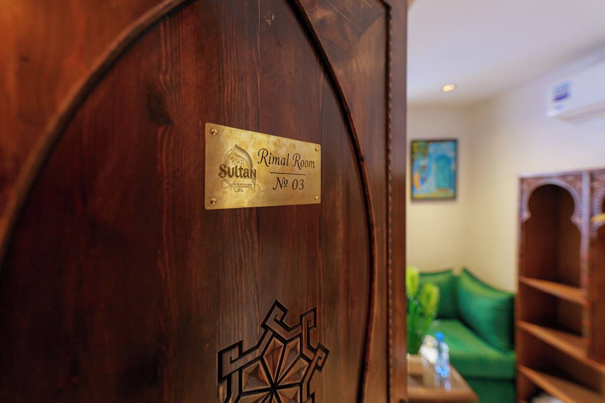 Uma porta de madeira com uma placa de latão que diz 'Rimal Room No 03' e um desenho geométrico.