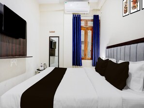 A hotel room with a bed, a TV, an air conditioner, a mirror, and a window with curtains. - Deluxegopal Singh Niwas (Varanasi)