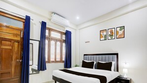 A bedroom with a bed, curtains, a window with bars, an air conditioner, and artwork on the wall. - Deluxegopal Singh Niwas (Varanasi)