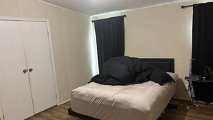 Un dormitorio con cama, armario, escritorio con ordenador y ventana con cortinas.