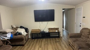 Un salón con un televisor de pantalla plana montado en la pared, un mueble de entretenimiento negro, dos sofás marrones y suelo de madera.